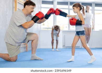 Father and girl engaged during training, boxing classes. Parent helps his daughter master basic wrestling skills. Parent coach in teaches child protection during wrestling and dueling, martial arts - Powered by Shutterstock