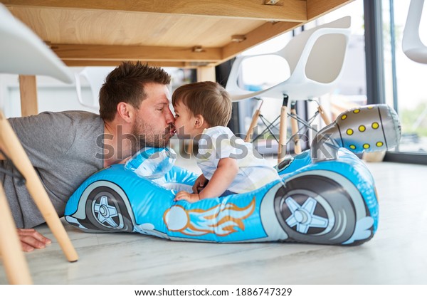 Father gives his son a kiss in the child\'s car while\
playing in the living\
room