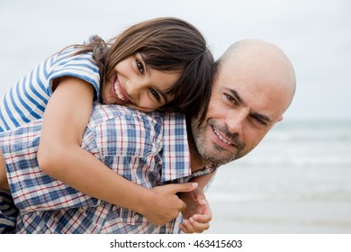 Father Giving His Daughter A Piggy Back Ride On The Beach In A Cloudy Day