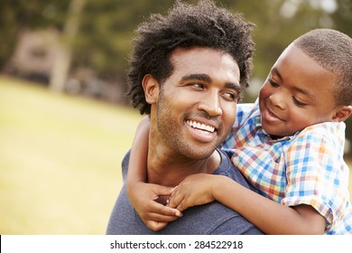 Father Giving Son Piggyback Ride In Park