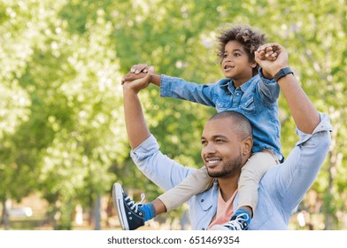 Father giving son ride on back at park. Portrait of happy african father giving son piggyback ride on his shoulders and looking up. Cute black boy with dad playing outdoor. Father day concept.