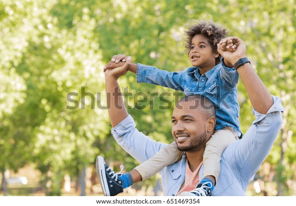 父は公園で息子を乗せて帰る 子どもを肩に乗せて上を見上げるアフリカの幸せな父親のポートレート お父さんとアウトドアで遊んでるかわいい黒い男の子 父の日のコンセプト の写真素材 今すぐ編集