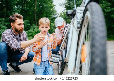 Father Giving Tool Son For Reparing Bike Outdoor. Dad, Grandad And School Age Grandson Son Fixing Bicycle At Summer Green Park Outside. Happy Family Relation Different Generation Concept.