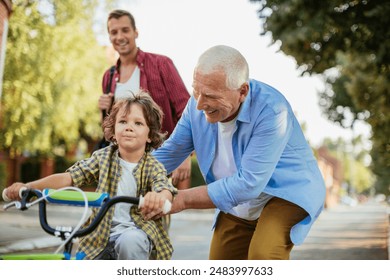 Father and grandfather teaching young boy to ride a bike on residential street - Powered by Shutterstock