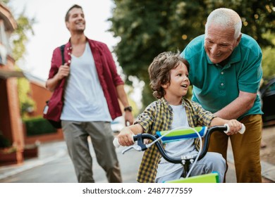 Father and grandfather teaching young boy to ride a bike on residential street - Powered by Shutterstock