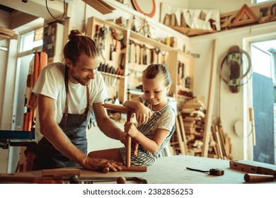 Father guiding his daughter in crafting wood in their workshop - Powered by Shutterstock