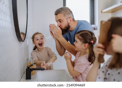 Father having fun blowing bubbles from soap in bathroom with his little daughters.
