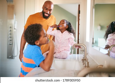 Father Helping Children To Brush Teeth In Bathroom At Home - Powered by Shutterstock