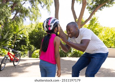 Father helping daughter with helmet, preparing for bike ride in park. Parenting, bonding, safety, family, outdoors, recreation - Powered by Shutterstock