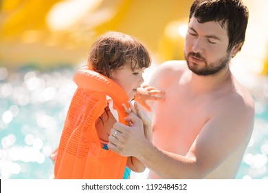 Father Helping His Cute Toddler Daughter Wuth Her Life Jacket In Outdoors Swimming Pool In Water Park (aquapark), Safety At The Water.