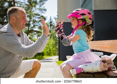 Father helping his daughter in helmet to wear protective pads for roller skates. Happy family spending time together, giving high five. Sunny summer day on suburb street.  - Powered by Shutterstock