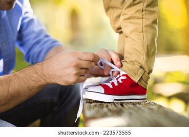 Father is helping his son to tie his shoes in summer nature