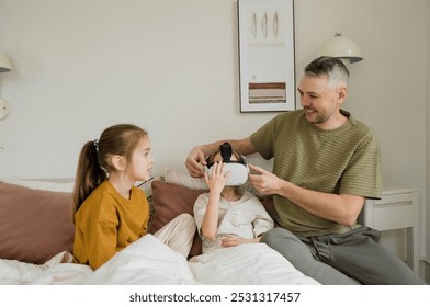 A father helps his daughter put on a VR headset, while his other daughter watches with excitement. The scene captures a heartwarming moment of family bonding and technological exploration. - Powered by Shutterstock