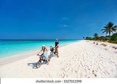 Father and her little daughter riding bikes at tropical beach having fun together