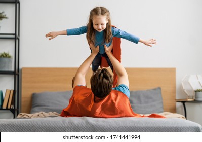 Father and his child playing together. Girl and dad in Superhero costume. Daddy and kid having fun, smiling and hugging. Family holiday and togetherness. - Powered by Shutterstock