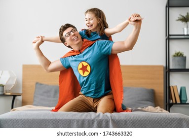 Father and his child playing together. Girl and dad in Superhero costume. Daddy and kid having fun, smiling and hugging. Family holiday and togetherness.