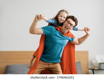 Father and his child playing together. Girl and dad in Superhero costume. Daddy and kid having fun, smiling and hugging. Family holiday and togetherness. - Powered by Shutterstock