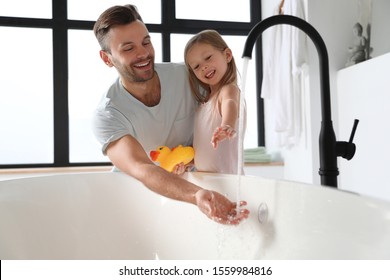 Father with his cute little daughter filling tub in bathroom