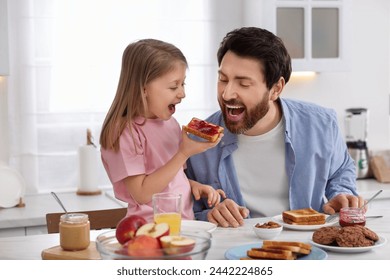 Father and his cute little daughter having fun during breakfast at table in kitchen - Powered by Shutterstock