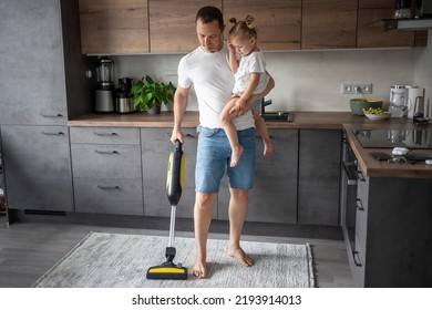 Father with his daughter on his hands vaccuming the floor in the modern home kitchen. High quality photo - Shutterstock ID 2193914013