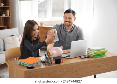 Father and his daughter putting money into piggy bank at home. Tuition fees concept - Powered by Shutterstock