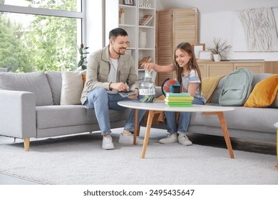 Father and his daughter putting money into jar with text COLLEGE at home. Tuition fees concept - Powered by Shutterstock