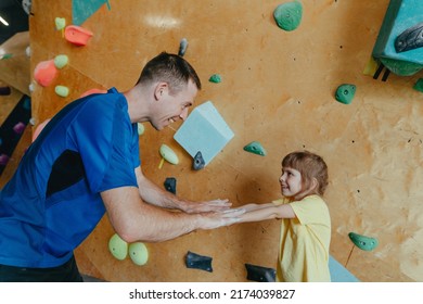 Father And His Daughter Rock Climbers Training In A Modern Indoor Rock Climbing Gym. Male Instructor Giving High Five To Little Girl Preschooler On A Private Coach Class. Family Sport Activities. 