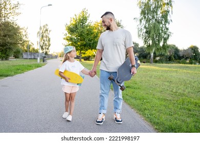 Father and his daughter walk with the skateboards in their hands in a park at the sunny day - Powered by Shutterstock