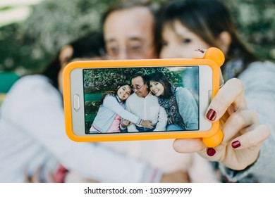 
A father with his daughters sitting on a stone bench, taking themselves some photographs. Father's day. Relaxed autumn day in family outdoors. Lifestyle portrait.

