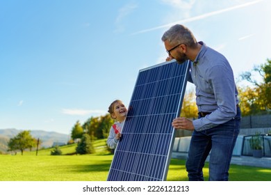 Father with his little daughter catching sun at solar panel,charging at their backyard. Alternative energy, saving resources and sustainable lifestyle concept. - Powered by Shutterstock