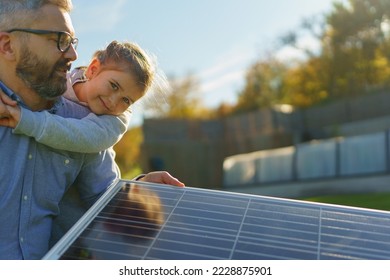 Father with his little daughter catching sun at solar panel,charging at their backyard. Alternative energy, saving resources and sustainable lifestyle concept. - Powered by Shutterstock