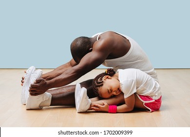 Father and his little daughter stretching knees and backs on the floor at home, folding themselves. Pained faces, feeling tension in ligaments and sinews. - Powered by Shutterstock