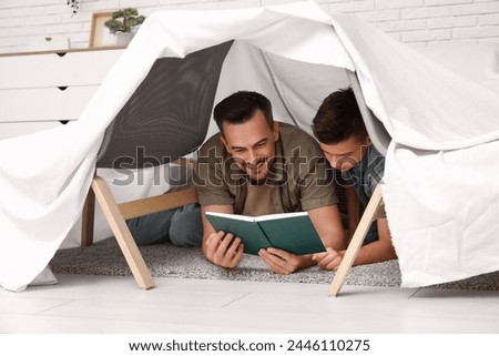 Father and his little son reading book in hovel at home