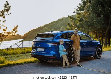 Father and his son charging electric car during their trip. - Shutterstock ID 2323448579
