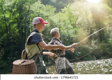 A father and his son fly fishing in summer on a beautiful trout river with clear water
