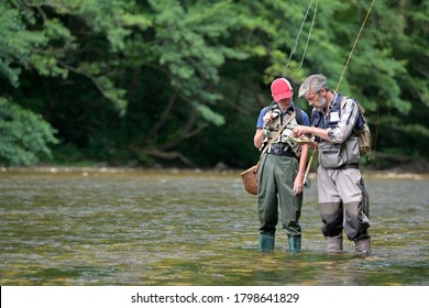 A father and his son fly fishing in summer on a beautiful trout river with clear water