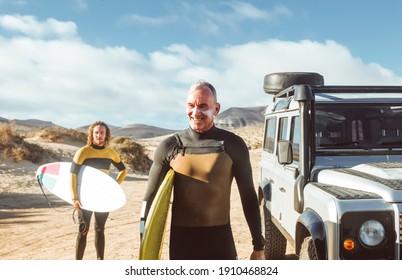 Father and his son getting ready to go surfing in the sea- Men wearing wetsuits, carrying their surfboards - Two friends standing next a 4x4 car - Powered by Shutterstock