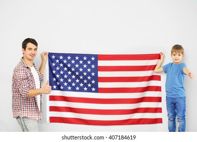Father and his son holding    USA flag on the light blue wall