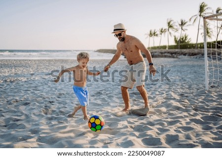 Father with his son plaing football on the beach.
