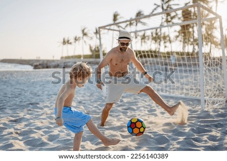 Father with his son plaing football on the beach.