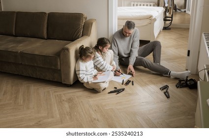 A father and his two daughters are having a creative and fun time together. The father is sitting on the floor, watching as his daughters draw with colorful markers.  - Powered by Shutterstock