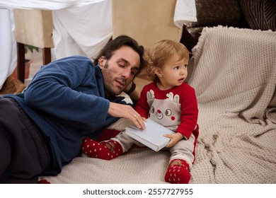 A father and his young child share a quiet moment reading a book in a homemade pillow fort, fostering a sense of warmth and family bonding. - Powered by Shutterstock