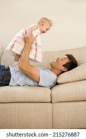 Father Holding Up Baby Girl (9-12 Months), Lying On Sofa, Side View