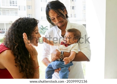 Father holding baby when smiling mother making funny face to set her little son laughing