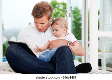 Father Holding Child While Using Digital Tablet At Home