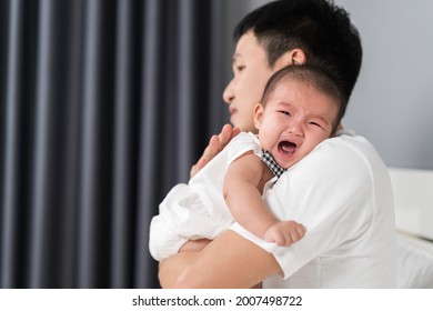 Father Holding Crying Baby On A Bed