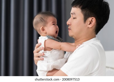 Father Holding Crying Baby On A Bed