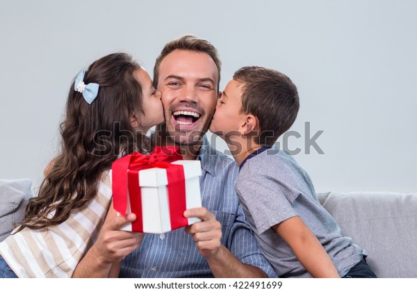 Father holding a gift and receiving kisses from\
son and daughter