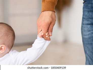 Father Holding Hand Of Little Baby Toddler Helping Child Make First Steps Standing At Home. Daddy's Support. Cute Family And Fatherhood Moments Concept. Cropped, Closeup