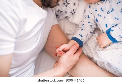Father holding hand of a sleeping toddler boy in bed at home.